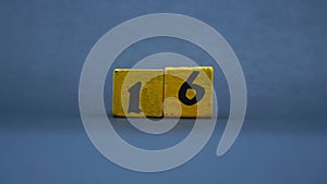 Wooden block with number 16. Yellow color on dark background
