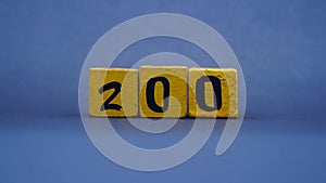 Wooden block with number 200. Yellow color on dark background