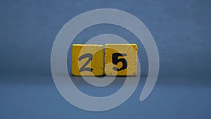 Wooden block with number 25. Yellow color on dark background