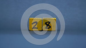 Wooden block with number 28. Yellow color on dark background