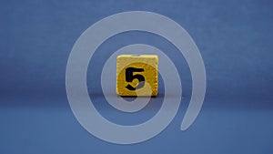 Wooden block with number 5. Yellow color on dark background