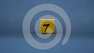 Wooden block with number 7. Yellow color on dark background