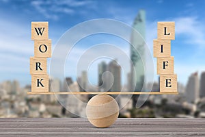 Wooden block with words work and life on wooden seesaw balancing on wood desk with city background