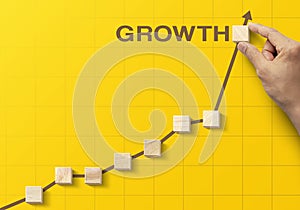 Wooden blocks arranged in an increasing graph with the word GROWTH on yellow background. Business growth, career growth or growth