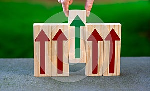 Wooden blocks with arrows pointing upwards. Hand selecting one block. Symbol for making the right decision