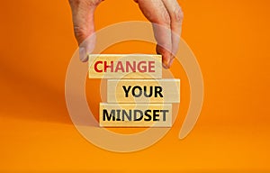 Wooden blocks form the words `change your mindset` on orange background. Male hand. Business concept, copy space