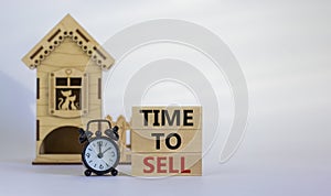 Wooden blocks form the words `time to sell` near miniature house. Black alarm clock. Beautiful white background. Business concep