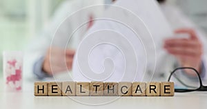 Wooden blocks with inscription healthcare on background of doctor