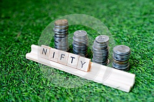 Wooden blocks with NIFTY written on them with a growing stack of coins behind it sitting on grass