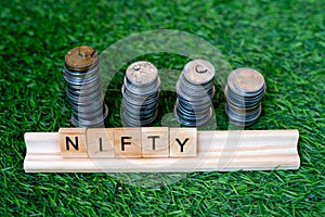 Wooden blocks with NIFTY written on them with a growing stack of coins behind it sitting on grass