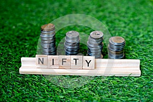 Wooden blocks with NIFTY written on them with a growing stack of coins behind it sitting on grass