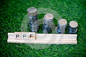 Wooden blocks with PPF for public provident fund called out on them and a stack of coins stacked like a growing graph on photo