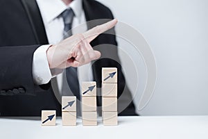 Wooden blocks with red arrow icon, businessman in suit pointing up against white background, business profit success concept