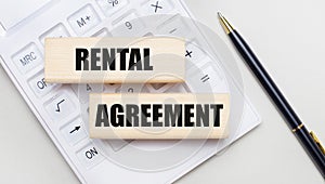 Wooden blocks with the RENTAL AGREEMENT Iie on a light background on a white calculator. Nearby is a black handle. Business