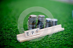 Wooden blocks spelling EPF with a stack of coins growing in size set on grass