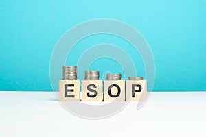 wooden blocks with text ESOP and coins on wooden table. copy space. blue background