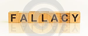 Wooden Blocks with the text: FALLACY. The text is written in black letters and is reflected in the mirror surface of the table.