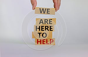 Wooden blocks with text `we are here to help`. Male hand. Beautiful white background, copy space. Business concept