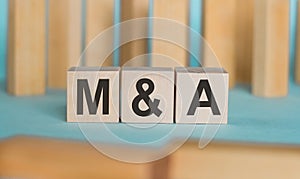 Wooden blocks with text M and A on light blue paper, business concept. MA - short for mergers and acquisitions