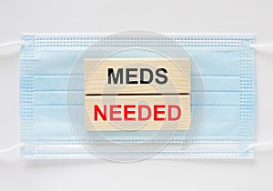 Wooden blocks with text Meds Needed lying on the mask