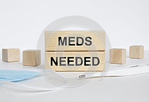 Wooden blocks with text Meds Needed with mask and thermometer