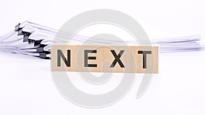 wooden blocks with text NEXT on white table, stack white paper on background
