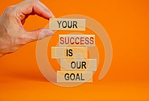 Wooden blocks with text `your success is our goal`. Male hand. Beautiful orange background, copy space. Business concept