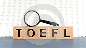 On wooden blocks under a magnifying glass text: TOEFL. Educational concept. TOEFL - words from wooden blocks with letters, Test of