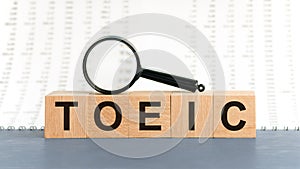 On wooden blocks under a magnifying glass text: TOEIC. Educational concept