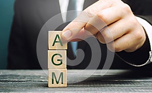 Wooden blocks with the word AGM - Annual general meeting. Mandatory yearly gathering of a company`s interested shareholders.
