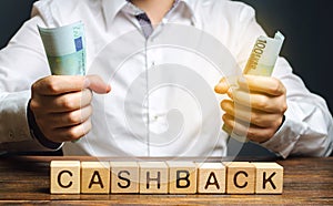 Wooden blocks with the word Cashback and money in the hands of a businessman. Bonus program to attract customers and increase