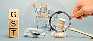 Wooden blocks with the word GST, money and a supermarket trolley with a judge`s gavel. Tax, which is imposed on the sale of goods