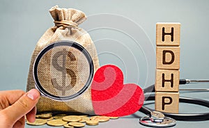 Wooden blocks with the word HDHP and money bag with dollar sign. High-deductible health plan concept. Health insurance plan with