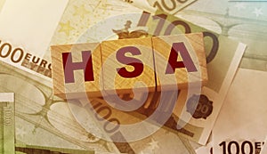 Wooden blocks with the word HSA standing for Health savings account put on 100 Euro bills. Healthcare, life insurance