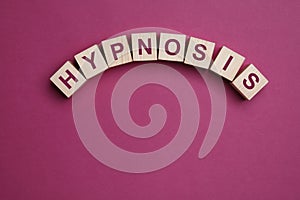 Wooden blocks with word HYPNOSIS on magenta background