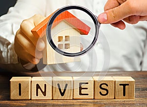 Wooden blocks with the word Invest and house in the hands of a businessman. The concept of investing in real estate construction.