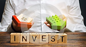 Wooden blocks with the word Invest and houses in the hands of a businessman. The concept of investing in real estate construction