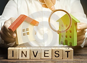 Wooden blocks with the word Invest and houses in the hands of a businessman. The concept of investing in real estate construction