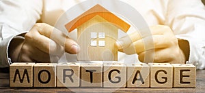 Wooden blocks with the word Mortgage and house in the hands of a businessman. The concept of buying a home on credit. Loan for