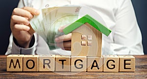 Wooden blocks with the word Mortgage and money in the hands of a businessman. The concept of buying a home on credit. Loan for