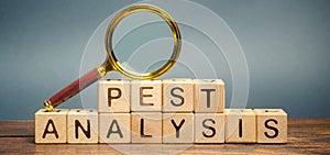 Wooden blocks with the word PEST analysis and a magnifying glass. Political, economic, socio-cultural and technological analysis. photo
