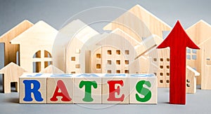 Wooden blocks with the word rates, up arrow and miniature houses. The concept of high interest rates on mortgages. Real estate.