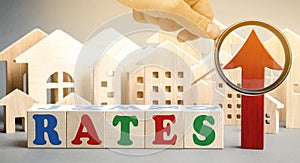 Wooden blocks with the word rates, up arrow and miniature houses. The concept of high interest rates on mortgages. Real estate.