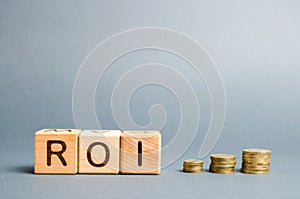 Wooden blocks with the word ROI and coins. High level of business profitability. Return on investment, invested capital, rate.