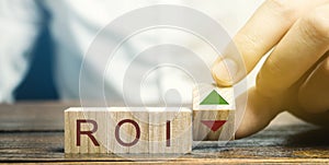 Wooden blocks with the word ROI and green arrow up. High level of business profitability. Return on investment, invested capital,