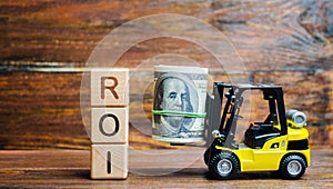 Wooden blocks with the word ROI and money with forklift. Ratio between the net profit and cost of investment resulting from an photo