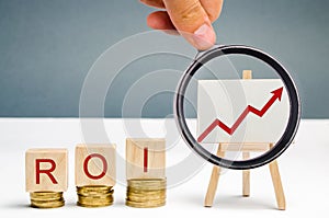 Wooden blocks with the word ROI and a poster with an arrow up. High level of business profitability. Return on investment,