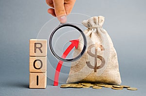 Wooden blocks with the word ROI and the up arrow with the money bag. High level of business profitability. Return on investment,