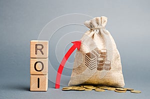 Wooden blocks with the word ROI and the up arrow with the money bag. High level of business profitability. Return on investment, photo