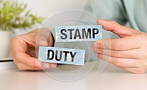 Wooden blocks with the word Stamp duty and hands. Taxes assessed during the transfer of real estate between two parties
